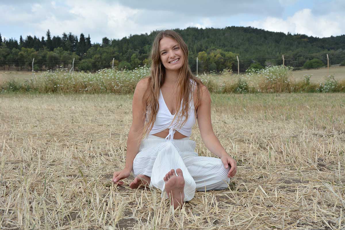 אריאל הרטמן יושבת בשדה חיטה קצור, מאחוריה חורש