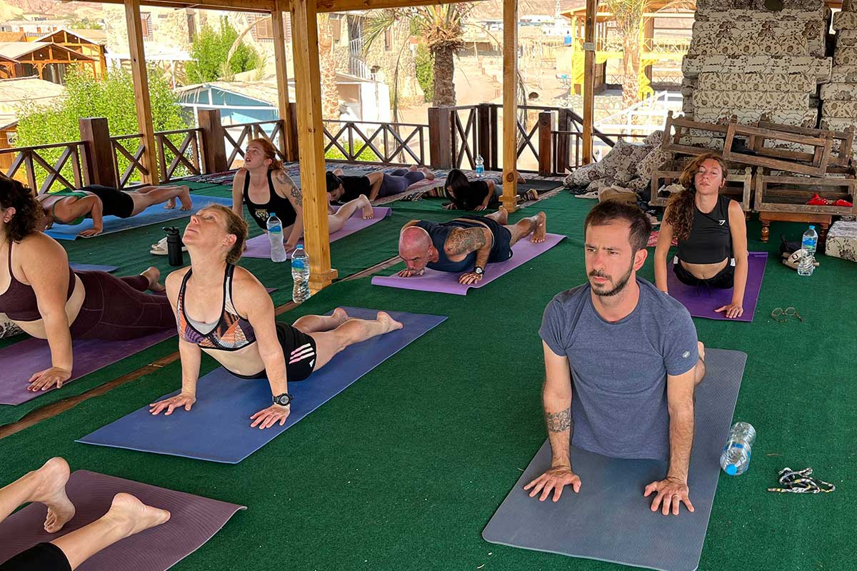 קבוצה מבצעת יוגה במבנה פתוח אך מקורה ברקע המדבר