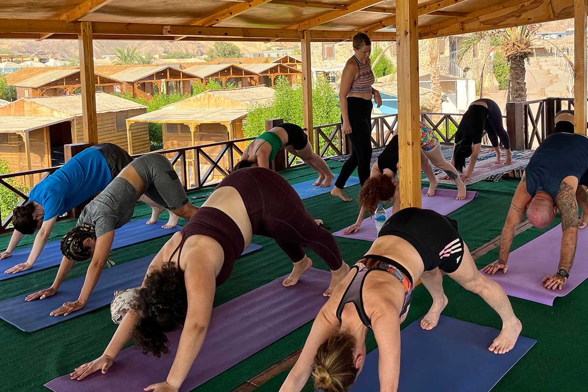 שיעור יוגה שמעבירה ברית לקבוצת מתאמנים ומתאמנות במשטח פתוח עם גג מעל